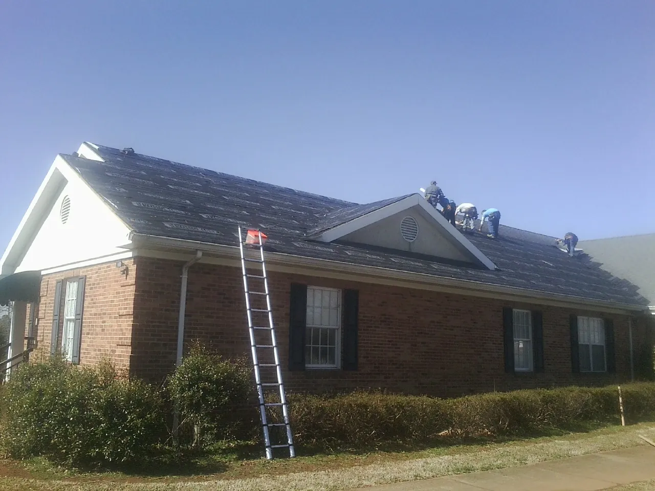 Crew tearing shingles off a brick ranch roof with a ladder set — Emergency Roof Repair work by our crew in West Wardsboro