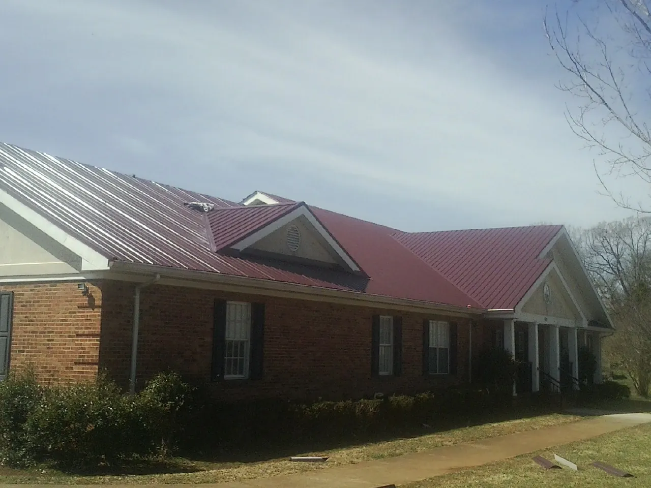 Red metal roof with gabled entries on a long brick building, from a Hail Damage Roof Repair job in West Wardsboro