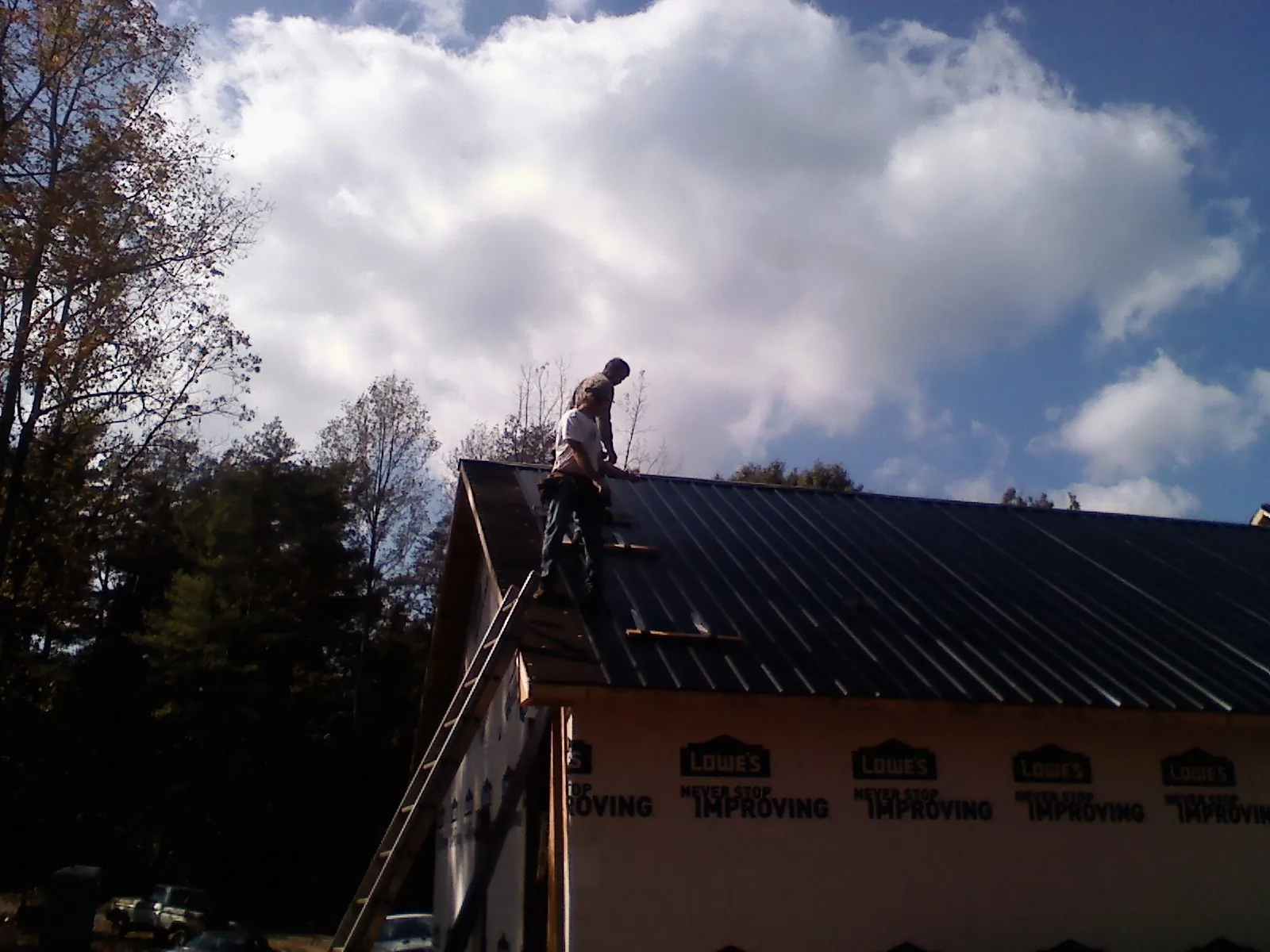 Roofer fastening dark metal panels high against a cloudy sky, from a Roof Inspection job in West Wardsboro