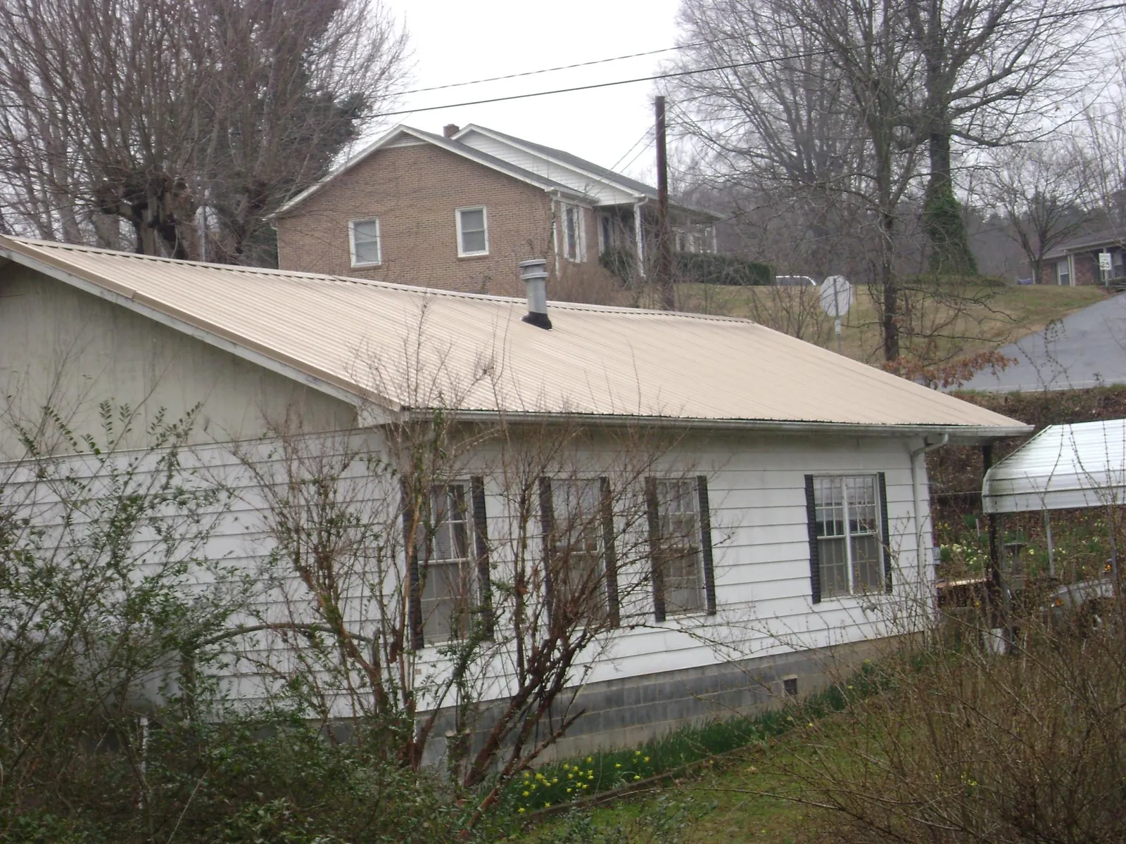 Tan metal roof on a white sided house set into a hillside — Commercial Roofing by Roofing Brothers in West Wardsboro